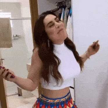 a woman in a white crop top and a blue skirt is standing in a bathroom .