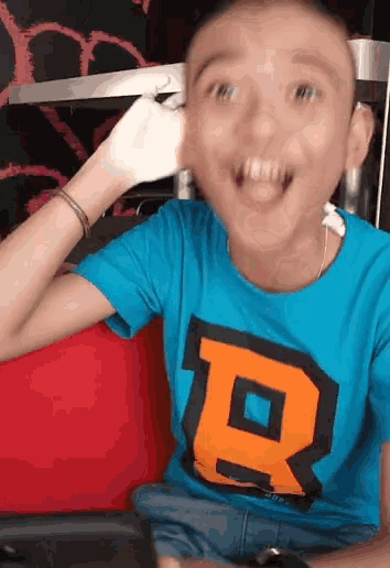 a boy wearing a blue shirt with the letter r on it is smiling