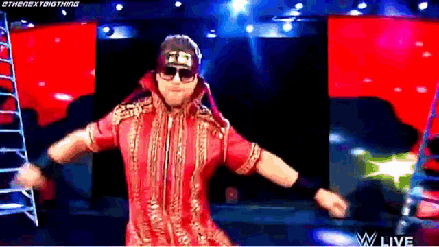 a wrestler in a red outfit and sunglasses is dancing on a stage .