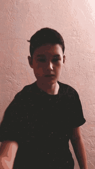 a young boy in a black shirt is standing in front of a pink wall