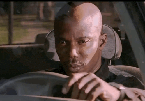 a man is sitting in the driver 's seat of a car looking at his watch .
