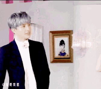 a man in a suit and bow tie stands in front of a framed picture of a woman