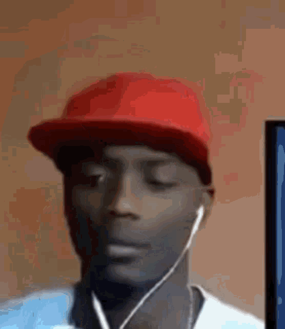 a man wearing a red hat and ear buds is looking at a computer screen .