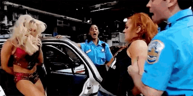 two women are standing in front of a police car while two police officers are standing behind them .