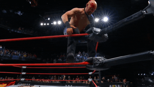 a wrestler is doing a handstand in a wrestling ring with a crowd in the stands watching