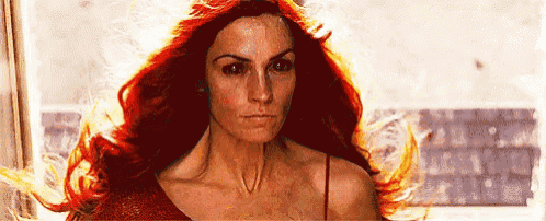 a woman with red hair is standing in front of a window and her hair is flying in the wind .