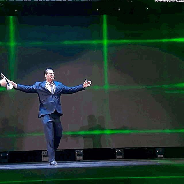 a man in a suit and tie is standing on a stage with his arms outstretched