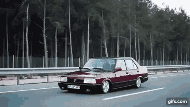 a red car is driving down a highway next to a forest