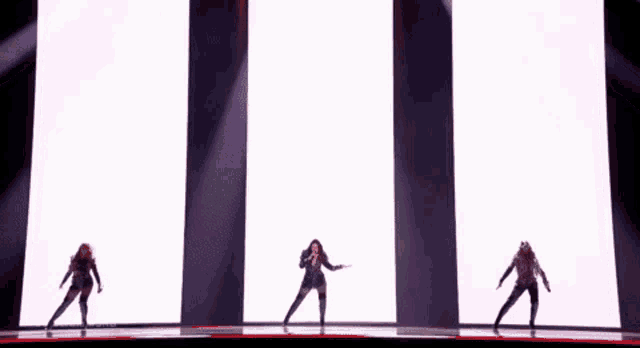 three women are dancing on a stage in front of a white screen