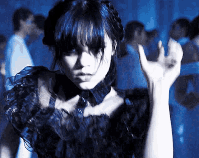a woman with blue hair and a black dress is dancing in a dark room
