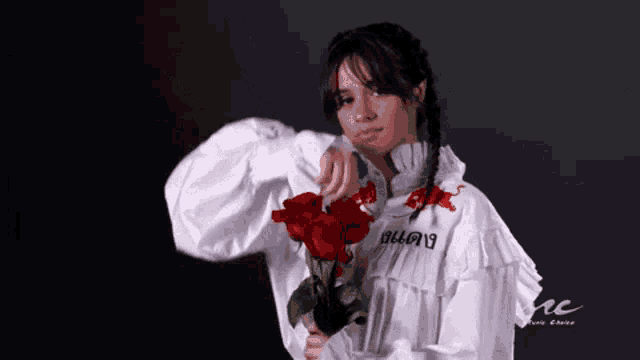 a woman in a white ruffled shirt is holding a bouquet of red roses