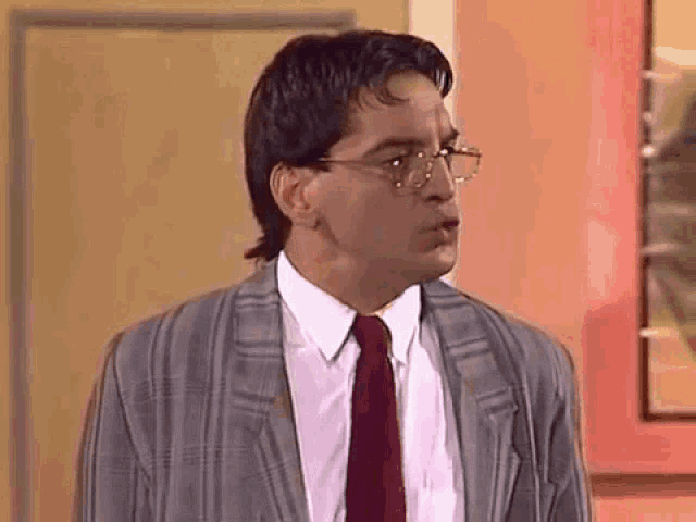 a man wearing glasses and a suit and tie is standing in front of a wall .