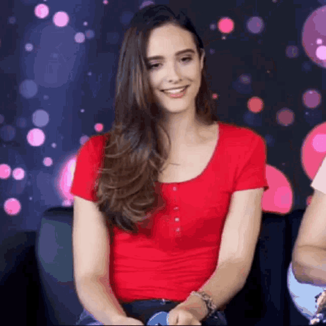 the woman is wearing a red shirt and smiling while sitting on a couch .