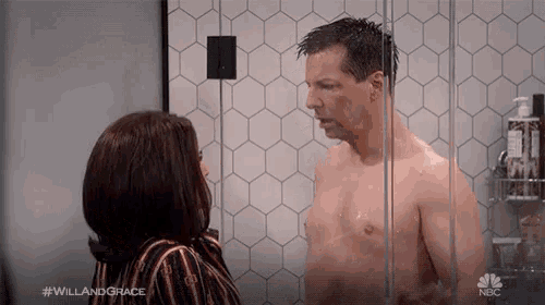 a man without a shirt is standing in a shower with a woman looking at him ..