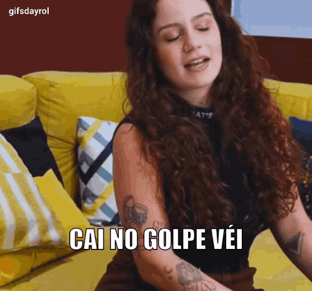 a woman sitting on a yellow couch with a tattoo on her arm says cai no golpe vei