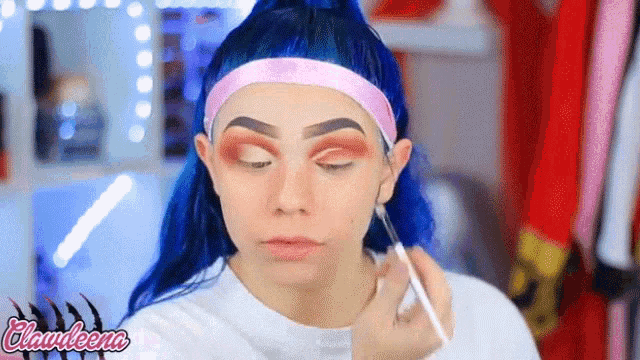 a woman with blue hair is applying makeup with a brush .