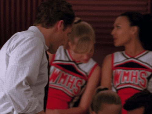 two cheerleaders from wmhs are talking to a man in a white shirt