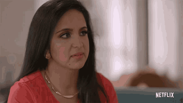 a woman wearing a red shirt and a gold necklace is sitting in front of a netflix logo .