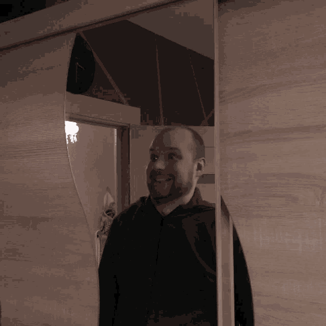 a man with a beard is smiling in front of a large mirror