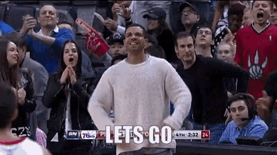 a man in a white sweater is dancing in front of a crowd at a basketball game and says let 's go .
