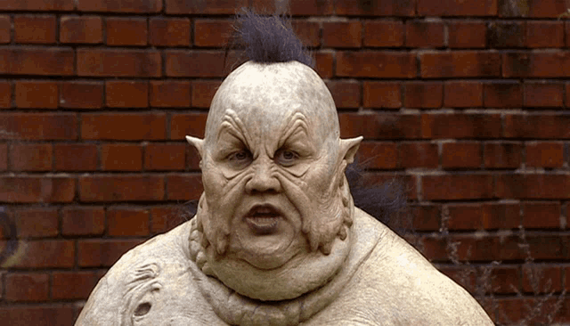 a statue of a man with a mohawk stands in front of a red brick wall