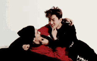 two young men are laying on a couch and one of them is wearing a black hat and a red jacket