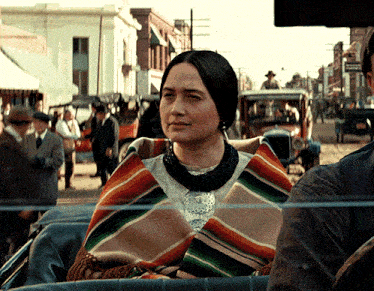 a woman wearing a colorful blanket sits in the back of a car