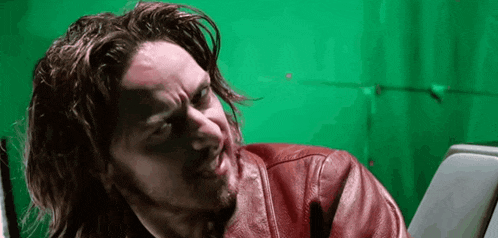 a man with long hair and a beard is wearing a red leather jacket against a green screen .
