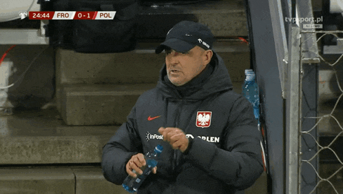 a man wearing a jacket that says orlen on it drinks water
