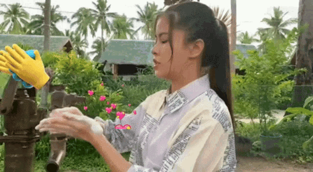 a woman is washing her hands in front of a water pump with a yellow glove behind her