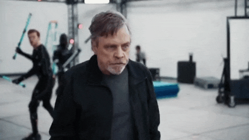 a man in a black jacket is standing in a room holding a lightsaber .