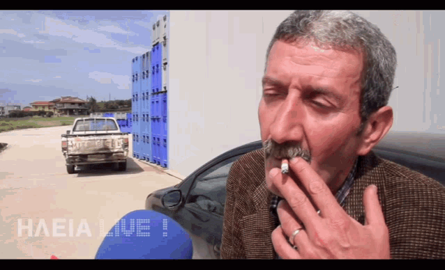 a man is smoking a cigarette in front of a truck that says haeia live