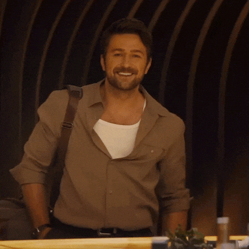 a man with a beard wearing a brown shirt is smiling and waving