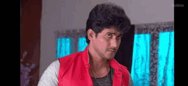 a young man in a red vest is standing in a living room .