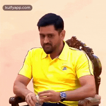 a man in a yellow shirt is sitting in a chair and drinking water .