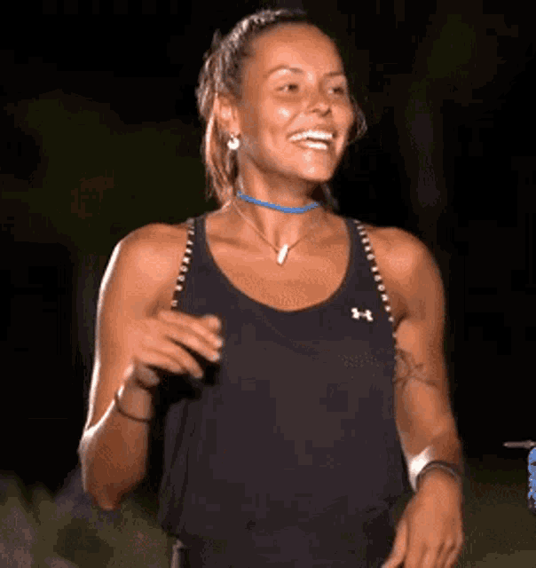 a woman wearing a black under armour tank top is smiling while standing in the dark .