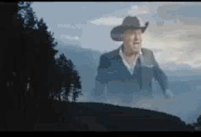 a man in a cowboy hat is standing on top of a hill in the fog .