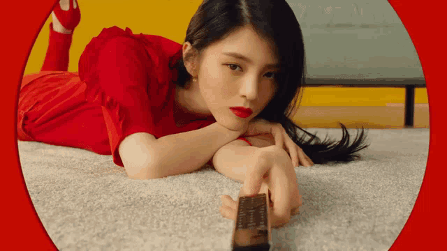 a woman in a red dress is laying on the floor and holding a remote control