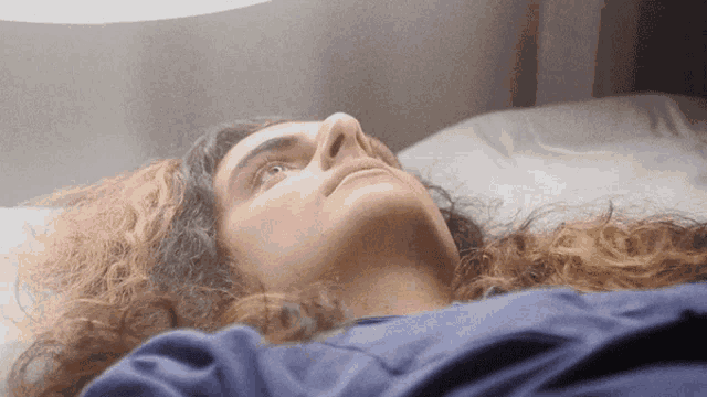 a woman with long curly hair is laying on a bed looking up