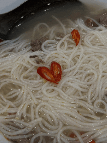 a close up of a bowl of noodles with red peppers on top
