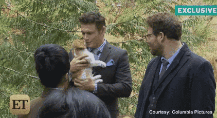 a man in a suit is holding a cat in front of a group of people and a sign that says exclusive on it