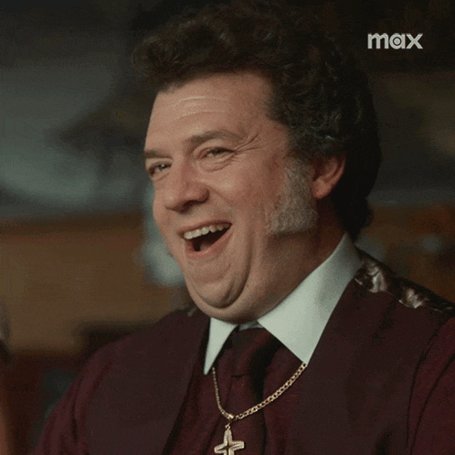 a man with a cross necklace is laughing in front of a screen that says max