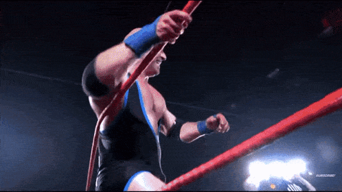 a wrestler in a black and blue singlet is holding a red rope