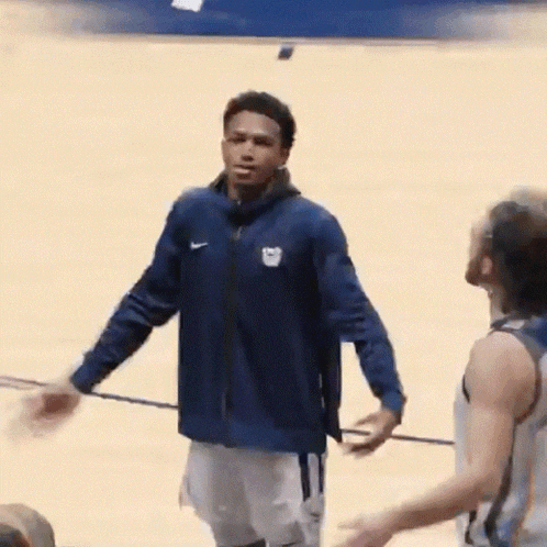 a man in a blue jacket is standing on a basketball court with another man .