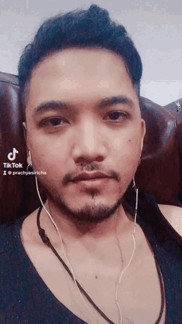 a man with a beard is wearing ear buds and a black tank top with tiktok written on the bottom