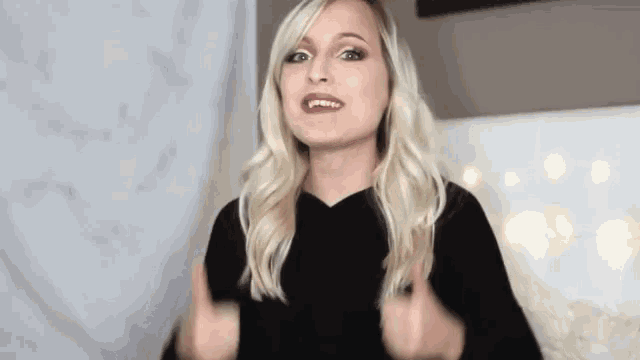 a woman is giving a thumbs up sign while wearing a black sweater .