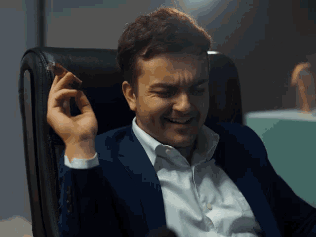 a man in a suit is smoking a cigar while sitting in a chair