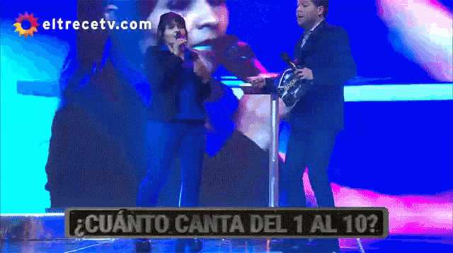 a man and a woman singing on a stage in front of a screen that says eltrecetv.com