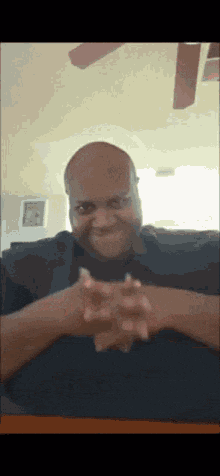 a bald man is sitting at a table with his hands folded