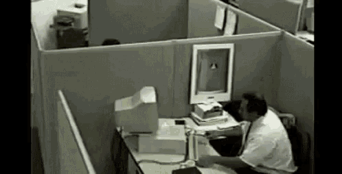 a man is sitting at a desk in a cubicle using a computer .